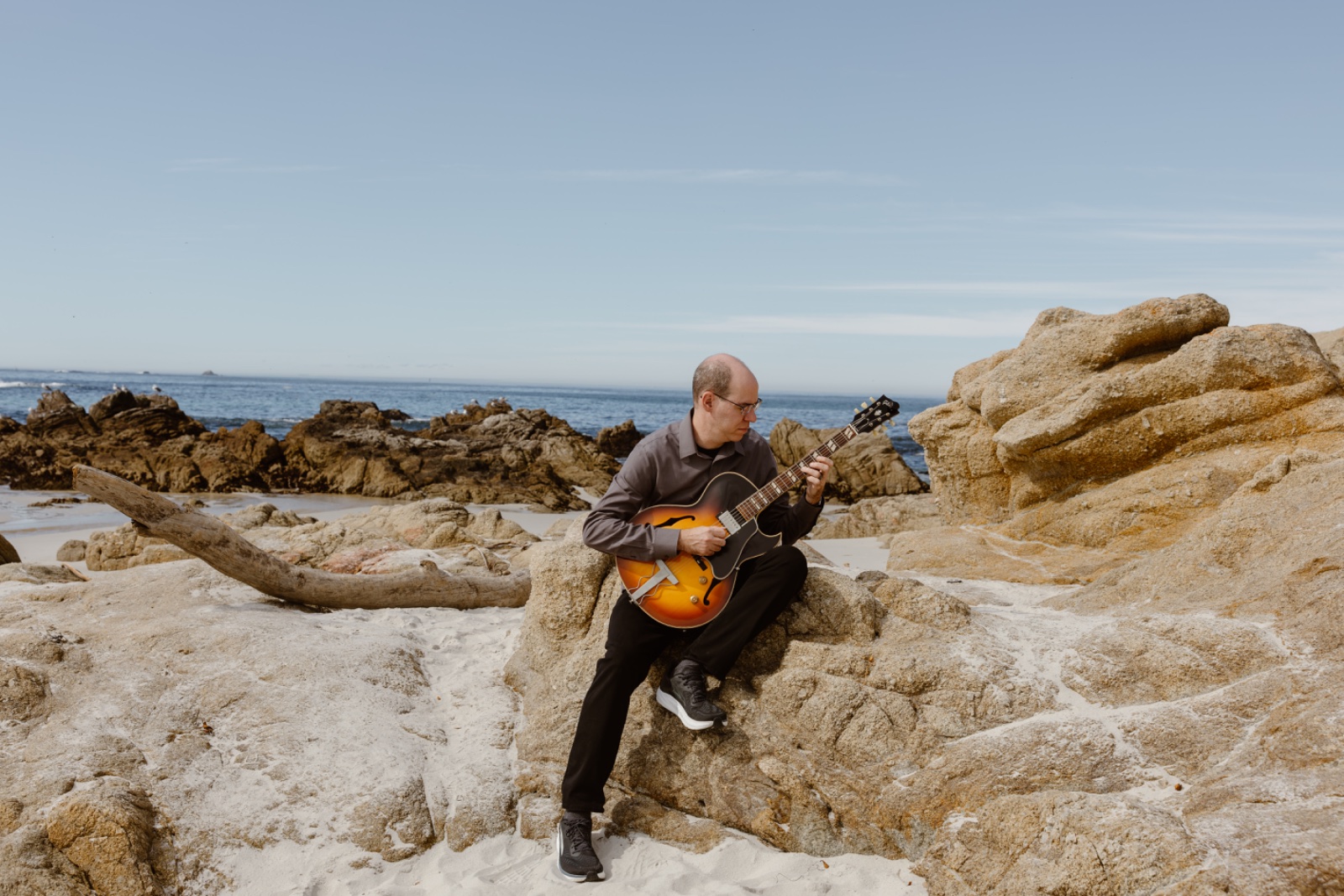 Marc playing guitar on the rocks by the ocean